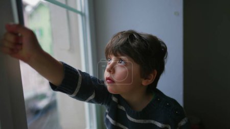 Photo for One little boy holding window knob wanting to open window from apartment second floor, child's safety concerns, security prevention - Royalty Free Image