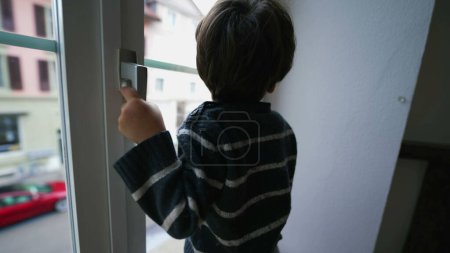 Téléchargez les photos : Enfant tenant dans le bouton de la fenêtre. Danger concept de petit garçon près du verre du deuxième étage appartement résidence - en image libre de droit