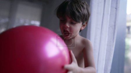 Foto de Un niño divertido inflando globo con la boca. Feliz niño mordiendo globo con dientes - Imagen libre de derechos