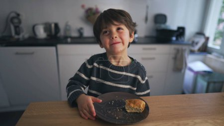 Foto de Lindo niño sonriendo a la cámara de pie en la cocina frente a la comida de plato. Un niño caucásico de 4 años - Imagen libre de derechos