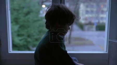 Photo for Sad Depressed Child with Melancholic Expression Looking Down, Sitting by Window at Home at Night - Royalty Free Image