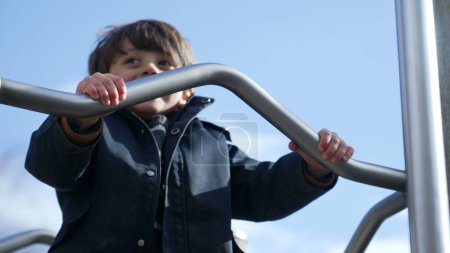 Photo for Joyful child sliding down metal bar at playground structure. Fun little boy enjoying outdoor exercise in childhood, wearing jacket during autumn day - Royalty Free Image