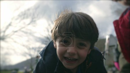 Foto de Niño emocionado sonriendo mientras gira en la rotonda en el patio de recreo durante la temporada de otoño, cara de primer plano de niño pequeño sintiendo emoción y felicidad - Imagen libre de derechos