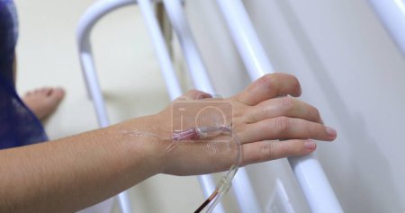 Téléchargez les photos : Hand connected to IV drip at hospital holding on bar - en image libre de droit
