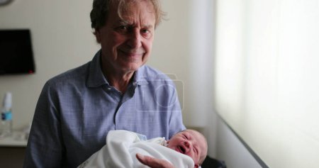 Foto de Grand-father smiling to camera while holding newborn baby - Imagen libre de derechos