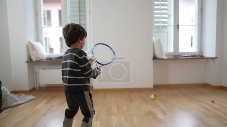 Photo for Rising Tennis Star/ Child's Tennis Play in empty Apartment Room, family relocating to new home. small boy exercises by hitting ball with racket into wall - Royalty Free Image