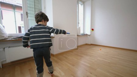 Foto de Ping-pong de interior para niños Ejercicio en la sala de apartamentos sin amueblar, golpear la pelota con raqueta contra la pared, reubicar el concepto de familia - Imagen libre de derechos
