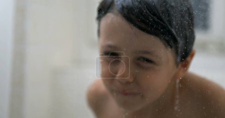 Photo for Droplets flowing in slow-motion with blurred child in background, small boy washing body during bath time in dreamy scene - Royalty Free Image