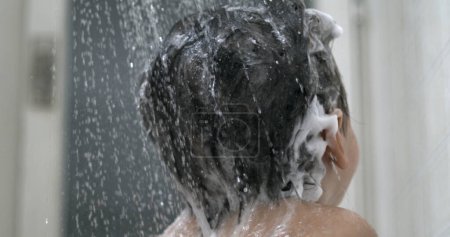 Foto de Agua que vierte en el champú para el lavado del cabello de los niños en una rutina de baño en cámara súper lenta. Cabeza del niño de la ducha del padre con la cabeza de la ducha - Imagen libre de derechos