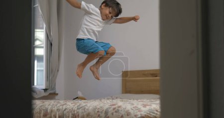 Photo for Excited happy child jumping up and down in bed in slow-motion. 1000 fps clip of little boy bouncing in bedroom - Royalty Free Image