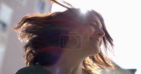 Foto de Mujer despreocupada sacudiendo el cabello en cámara súper lenta afuera a la luz del sol con bengalas. 800 fps clip de 30 años chica adulta sacude la cabeza hacia los lados - Imagen libre de derechos