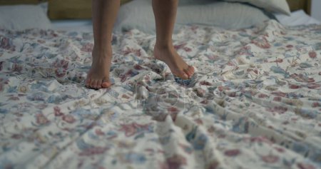 Téléchargez les photos : Gros plan de pieds d'enfant sautant dans le lit au ralenti avec des textures de feuille en mouvement - en image libre de droit