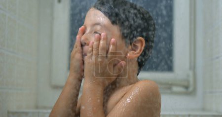 Téléchargez les photos : Gros plan sur le visage de l'enfant pendant le bain, des gouttelettes d'eau au mouvement super lent coulent dans la douche - en image libre de droit