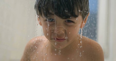 Photo for Close-up face of child face in shower bath in super slow-motion 800 fps smiling at camera, droplets of water flowing and splashing all around - Royalty Free Image