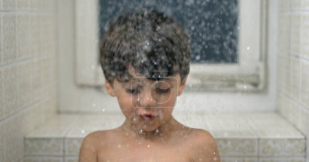 Téléchargez les photos : Un jeune garçon regardant des gouttelettes tombe au ralenti pendant le bain. pomme de douche chute d'eau - en image libre de droit
