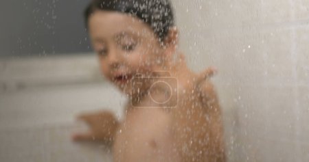 Téléchargez les photos : Élégance de l'heure du bain au ralenti - Des gouttelettes d'eau au premier plan avec la silhouette floue de lavage du jeune garçon en toile de fond - en image libre de droit