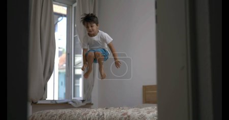 Téléchargez les photos : Joyeux enfant rebondissant sur le lit au ralenti super ultra, rampe de vitesse en 800 ips. jeune garçon sautant dans la chambre à coucher draps - en image libre de droit