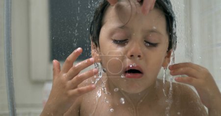 Photo for Displeased small boy underneath water shower head while grimacing in annoyance. kid in distress while bathing night routine in super slow-motion - Royalty Free Image