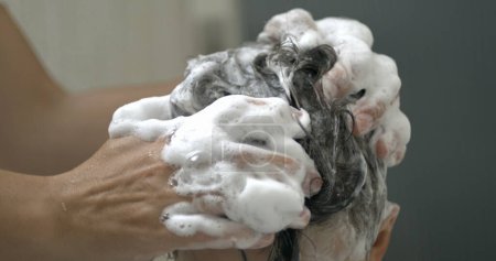 Foto de Los padres lavan el cabello del niño con champú en cámara lenta 800 fps. Joven chico frotando cabeza de niño - Imagen libre de derechos
