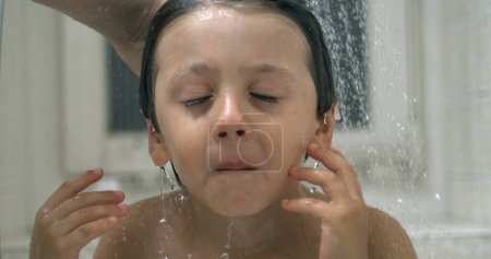 Photo for Displeased small boy underneath water shower head while grimacing in annoyance. kid in distress while bathing night routine in super slow-motion - Royalty Free Image