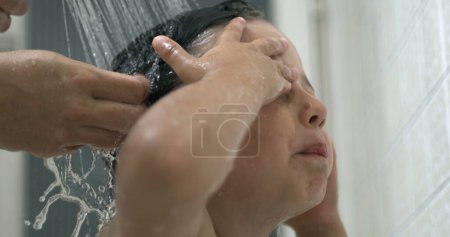 Photo for Dispelased child underneath shower head removing shampoo from eye, annoyed child during bath time routine - Royalty Free Image