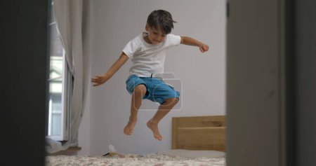 Téléchargez les photos : Excité enfant heureux sautant de haut en bas dans le lit au ralenti. 1000 fps clip de petit garçon rebondissant dans la chambre - en image libre de droit