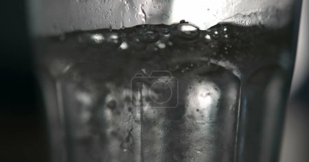 Téléchargez les photos : Eau bouillonnante Saupoudrer sur la surface en super ralenti, Verser une boisson rafraîchissante dans une tasse en verre transparent - en image libre de droit
