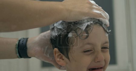 Téléchargez les photos : Enfant pleurant pendant que la main de la mère frotte ses cheveux avec un shampooing, émotion mécontente du petit garçon pendant la routine de nuit de bain au ralenti super - en image libre de droit