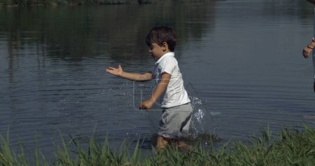 Photo for Small boy splashing water with hand by lake captured . Child enjoying nature connected with the natural world - Royalty Free Image