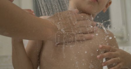 Foto de Madre lavando el cuerpo del niño debajo de la cabeza de la ducha, gotitas que fluyen y vierten en la piel del niño - Imagen libre de derechos