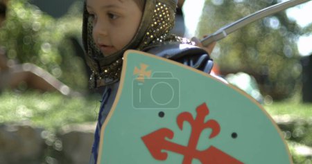 Téléchargez les photos : Petit garçon portant un costume médiéval traditionnel frappant avec l'épée et tenant bouclier capturé, rampe de vitesse - en image libre de droit
