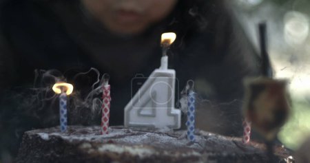 Foto de ¿Apagando las velas de cumpleaños de cuatro años? El cuarto deseo de cumpleaños del niño / las velas apagadas en la torta capturadas - Imagen libre de derechos