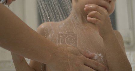Photo for Mother hand washing child's body underneath shower head in super slow-motion 800 fps, droplets flowing and pouring into young boy skin - Royalty Free Image