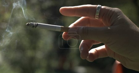 Foto de Dedo golpeando la ceniza de cigarrillo cayendo capturado. Acercamiento de la mano sosteniendo sustancia adictiva - Imagen libre de derechos