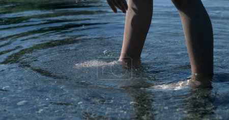 Téléchargez les photos : Jambes d'enfant debout à l'intérieur de l'eau de l'étang avec des ondulations coulant, personne en contact avec la nature - en image libre de droit
