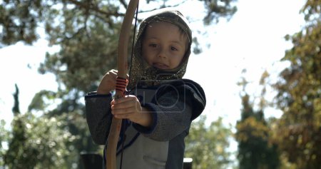 Téléchargez les photos : Petit garçon portant un costume médiéval lancer flèche tenant arc à l'extérieur capturé - en image libre de droit