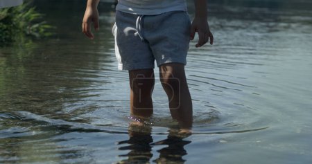 Photo for Small boy standing in pond water with ripples flowing . Child enjoying nature, contact with natural world, captured - Royalty Free Image