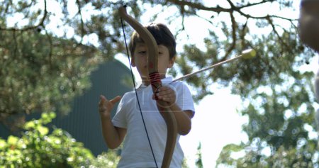 Foto de Chico joven disparando flecha con arco con el exterior. Niño juega con juguete capturado - Imagen libre de derechos
