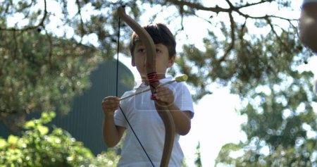 Photo for Young boy shooting arrow with bow with outside. Child plays with toy captured - Royalty Free Image
