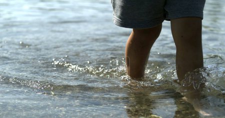 Téléchargez les photos : Bord du lac Treading Pieds minuscules, étapes de l'enfant le long des eaux côtières documenté - en image libre de droit