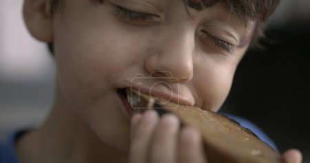 Téléchargez les photos : Rampe de vitesse du pain grillé mordant petit garçon - en image libre de droit
