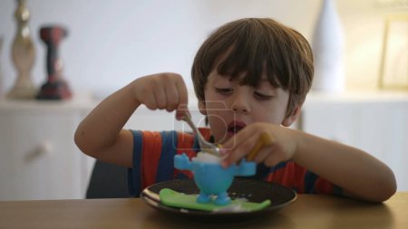 Téléchargez les photos : Un petit garçon mangeant un œuf à la coque molle, oeuf à la coque. Enfant mange repas léger par lui-même avec une cuillère - en image libre de droit