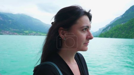 Téléchargez les photos : Femme debout à l'intérieur bateau voyageant à travers le lac et les montagnes. 30s femme jouissant d'une vue naturelle avec regard contemplatif - en image libre de droit