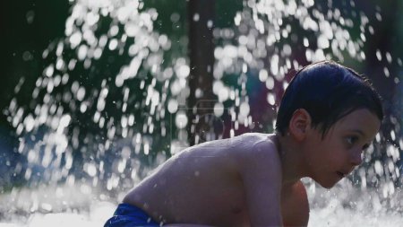 Téléchargez les photos : Enfant jouant à l'eau de piscine extérieure pendant la journée d'été, les gouttelettes d'éclaboussure de fontaine d'eau en arrière-plan à 120fps au ralenti - en image libre de droit