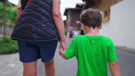 Photo for Back of little boy holding hands with grandmother walking in street. Family weekend lifestyle activity. Grandparent and grandson together - Royalty Free Image