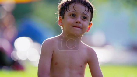 Foto de Feliz chico sentado afuera después de nadar en la piscina sonriendo. Niño sin camisa disfrutando del día cálido de verano - Imagen libre de derechos