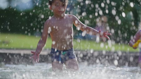 Téléchargez les photos : Enfant s'amusant pendant la chaude journée d'été, éclaboussant l'eau partout vers le haut au ralenti 120fps. Petit garçon profitant de la piscine - en image libre de droit