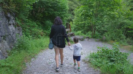 Téléchargez les photos : Dos de la mère et de l'enfant se tenant la main dans le sentier de la nature pendant la fin de semaine. Maman et petit garçon appréciant la journée de randonnée - en image libre de droit