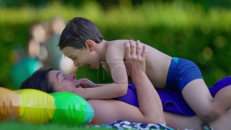 Photo for Happy mother and child laying down in outdoor grass after swimming at pool. Little boy and mom affectionate bonding and embrace moment - Royalty Free Image