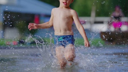 Photo for Child gleefully dashes in pool water on sunny summer day. Active little boy running causing splashes in 120fps slow-motion - Royalty Free Image